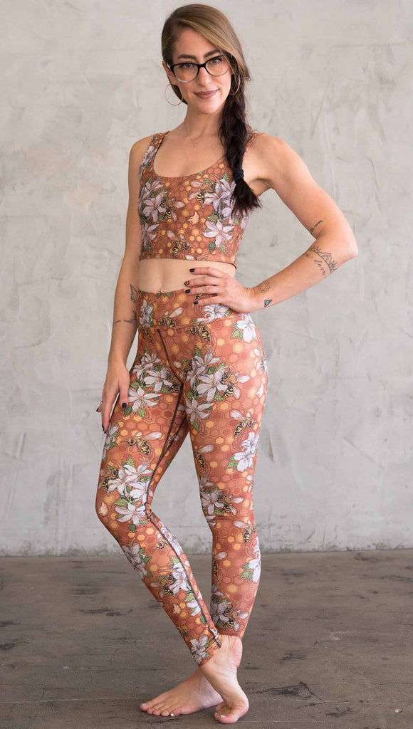 Full body side view of model wearing WERKSHOP Honeybees leggings in triathlon fabric. The artwork has clusters of honeybees and flowers.