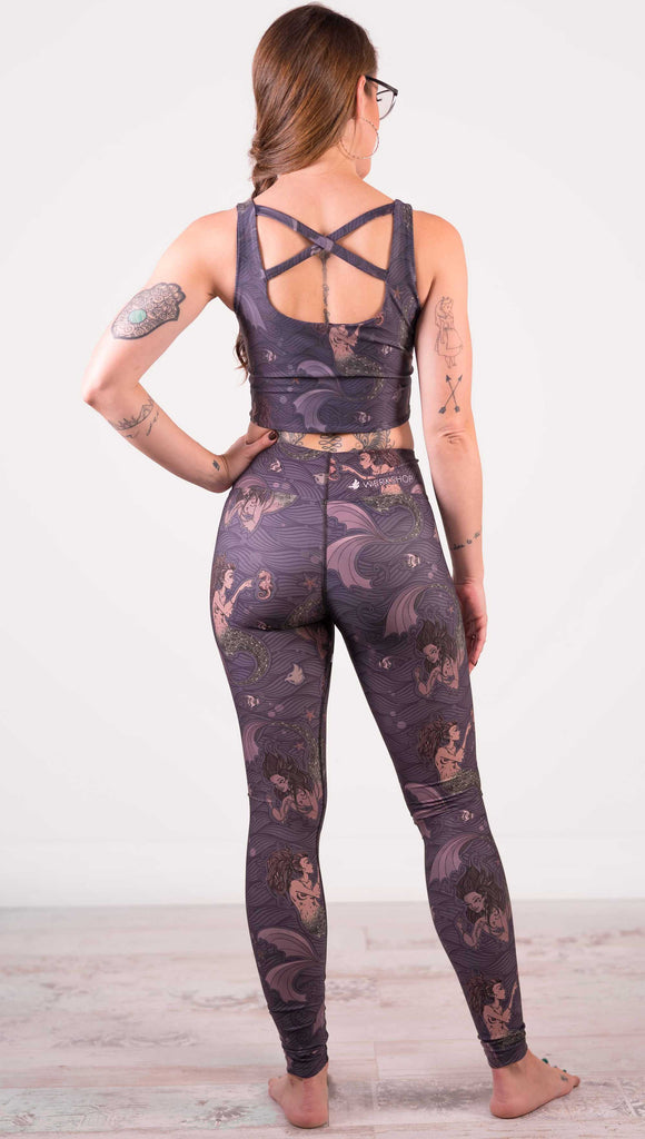 Model wearing WERKSHOP full length triathlon leggings with Original Mermaids artwork. The mermaids have small intricate details on the fins and are swimming with seahorses and angel fish over a dark blue background with waves.