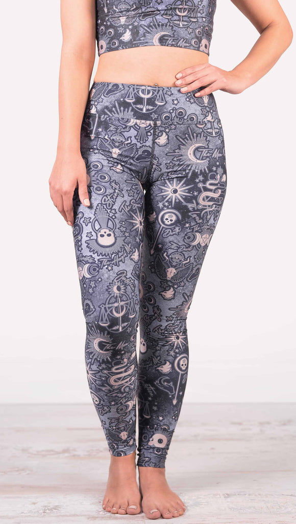 Model wearing WERKSHOP Tarot Full Length Triathlon Leggings. The blue/tarot artwork has skulls, snakes, moons and the names of multiple popular tarot cards like "Strength, Lovers, Death and The Hanged Man”. Triathlon leggings do not have pockets.