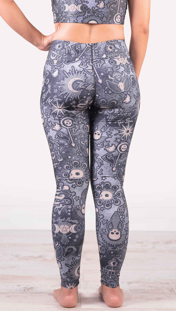 Model wearing WERKSHOP Tarot Full Length Triathlon Leggings. The blue/tarot artwork has skulls, snakes, moons and the names of multiple popular tarot cards like "Strength, Lovers, Death and The Hanged Man”. Triathlon leggings do not have pockets.