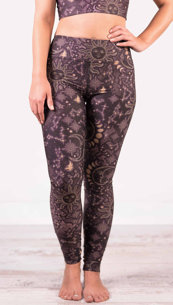 model wearing WERKSHOP Zodiac Full Length Triathlon Leggings. The zodiac themed artwork shows a hand-drawn sun and moon with the moon phases, shooting stars and all 12 zodiac constellations in gold over a dark purple background. Triathlon leggings do not have pockets.