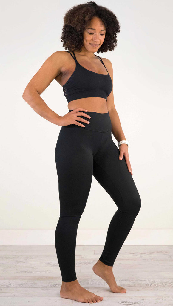 Full body front view of model wearing WERKSHOP Solid Black Athleisure Leggings with a small reflective eagle logo on the wearers left side calf