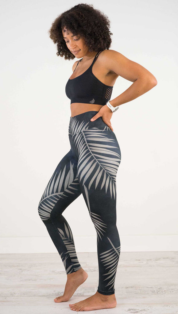 Full body side view of model wearing WERKSHOP Black Palms leggings. The leggings are printed with a mostly black watercolor effect with grayish palm frond silhouette wrapping the body.