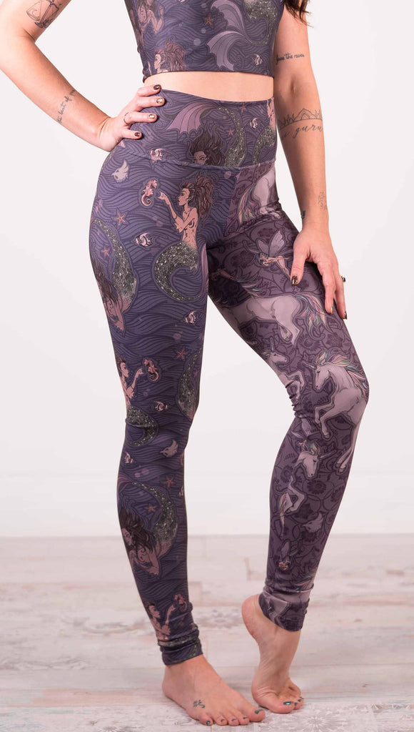 Model wearing WERKSHOP Mermaid and Unicorn Mashup Athleisure Leggings. The leggings feature mermaid artwork on the wearers right leg with a dark blue background and unicorns over a purple background on the wearer's left leg.