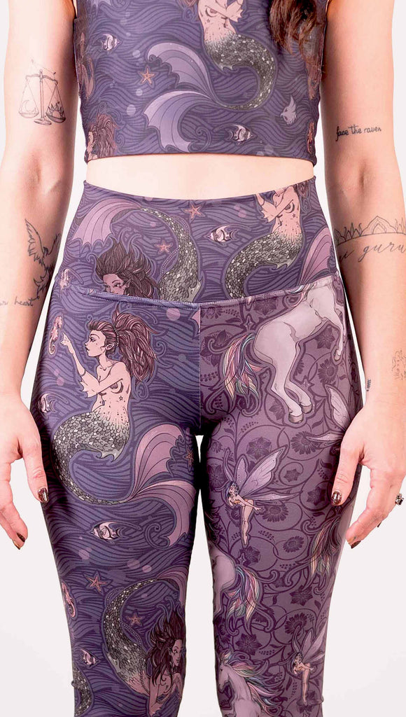 Model wearing WERKSHOP Mermaid and Unicorn Mashup Athleisure Leggings. The leggings feature mermaid artwork on the wearers right leg with a dark blue background and unicorns over a purple background on the wearer's left leg.