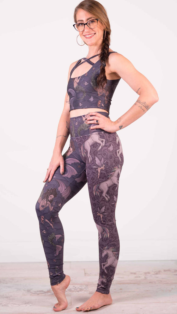 Model wearing WERKSHOP Mermaid and Unicorn Mashup Athleisure Leggings. The leggings feature mermaid artwork on the wearers right leg with a dark blue background and unicorns over a purple background on the wearer's left leg.