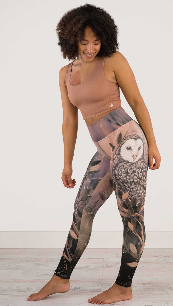 Full body front view of model wearing WERKSHOP Owls Athleisure Leggings. The leggings are printed with a whimsical barn owl on the thigh surrounded by swirls and leaves on a mauve and cream toned background.