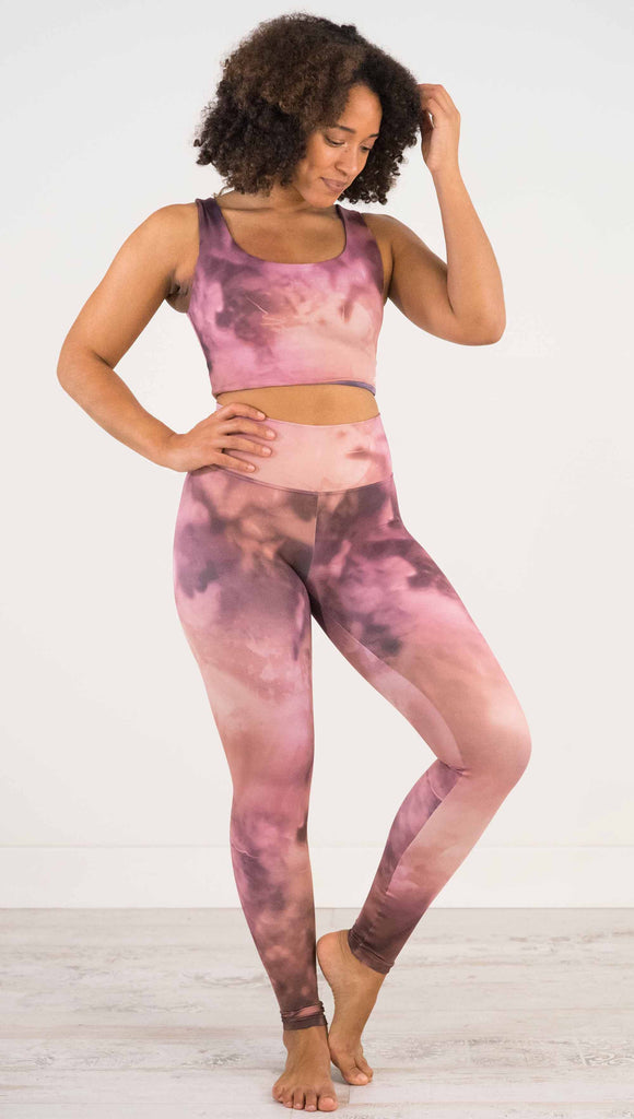 Full body front view of model wearing WERKSHOP Rose Quartz Athleisure Leggings. The leggings are printed with a warm rose/mauve and peachy watercolor effect with our eagle logo printed on the wearers outside left calf.