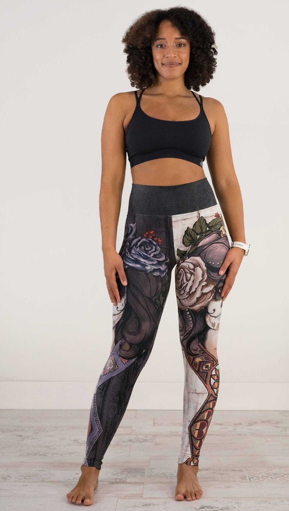 Full body front view of model wearing WERKSHOP Sugar Mashup Athleisure Leggings. The leggings are printed with original sugarskull themed artwork. The wearers left leg features "Remix", a romantic lighter version of the artwork with mauve roses in her hair. The other leg is printed with Dark Sugar, an edgier version of the same artwork with blue flowers in her hair. 