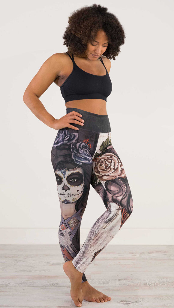 Full body front view of model wearing WERKSHOP Sugar Mashup Athleisure Leggings. The leggings are printed with original sugarskull themed artwork. The wearers left leg features "Remix", a romantic lighter version of the artwork with mauve roses in her hair. The other leg is printed with Dark Sugar, an edgier version of the same artwork with blue flowers in her hair. 