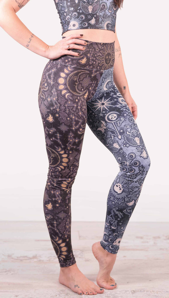 Model wearing WERKSHOP Zodiac and Tarot Mashed up Athleisure Leggings. The wearer’s right leg features zodiac themed artwork with the sun and moon with the moon phases, shooting stars and all 12 zodiac constellations in gold over a dark purple background. The left leg blue/tarot artwork has skulls, snakes, moons and the names of popular cards in the deck.