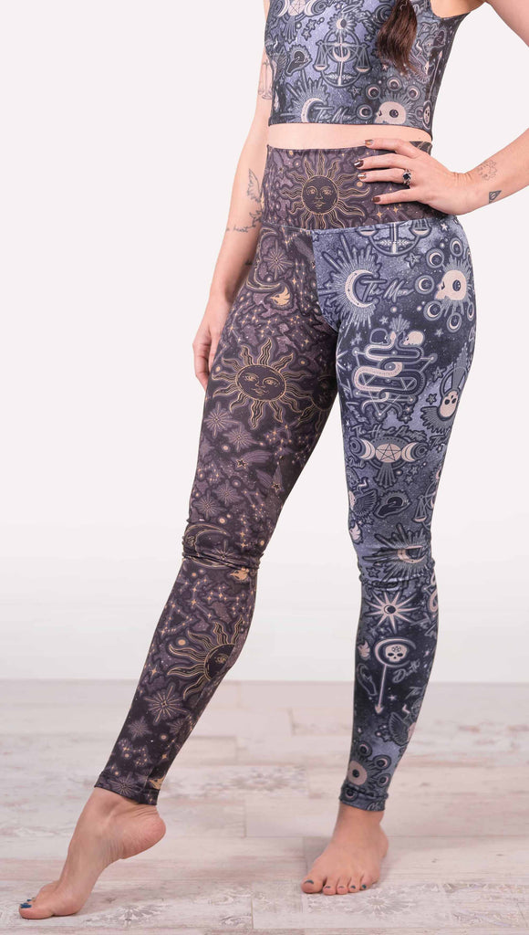 Model wearing WERKSHOP Zodiac and Tarot Mashed up Athleisure Leggings. The wearer’s right leg features zodiac themed artwork with the sun and moon with the moon phases, shooting stars and all 12 zodiac constellations in gold over a dark purple background. The left leg blue/tarot artwork has skulls, snakes, moons and the names of popular cards in the deck.