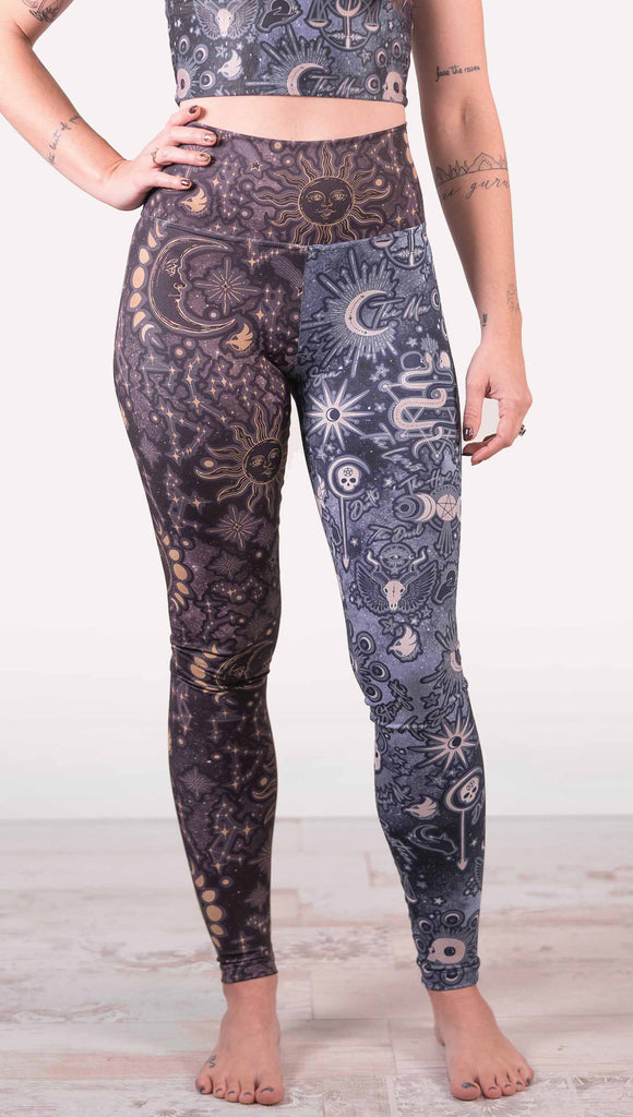 Model wearing WERKSHOP Zodiac and Tarot Mashed up Athleisure Leggings. The wearer’s right leg features zodiac themed artwork with the sun and moon with the moon phases, shooting stars and all 12 zodiac constellations in gold over a dark purple background. The left leg blue/tarot artwork has skulls, snakes, moons and the names of popular cards in the deck.