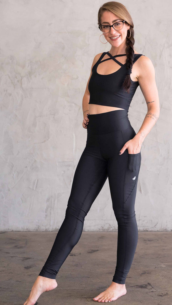 Full body side view of model wearing WERKSHOP featherlight leggings. Leggings have a small reflective eagle logo on the wearer's left pocket.