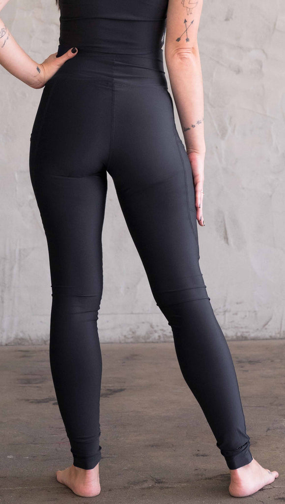 Waist down back view of model wearing WERKSHOP featherlight leggings. Leggings have a small reflective eagle logo on the wearer's left pocket.