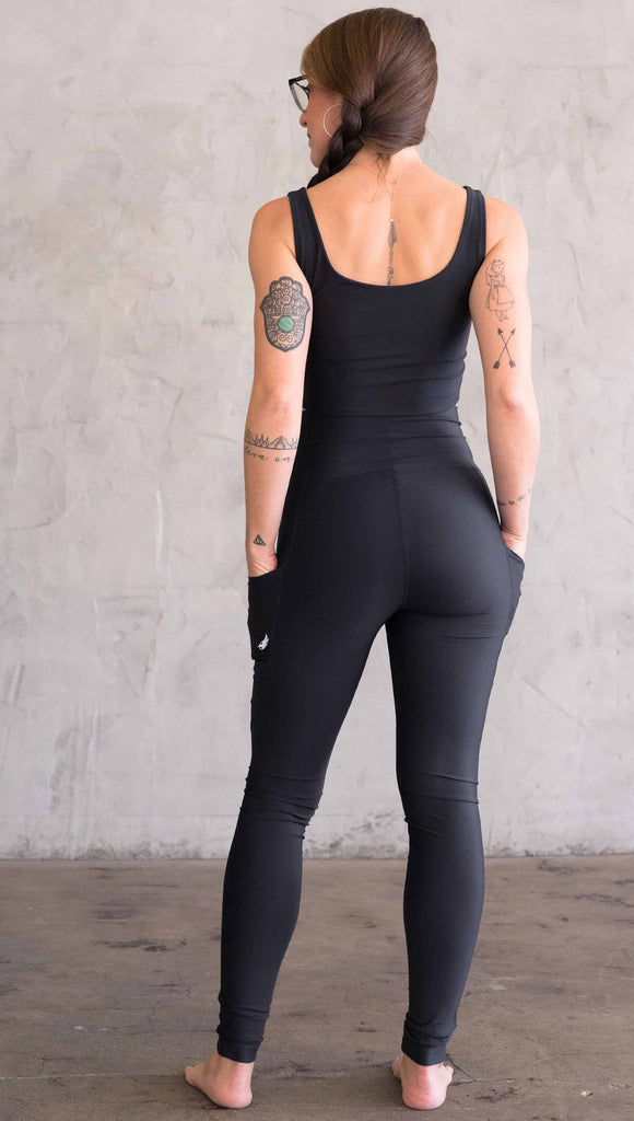 Full body back view of model wearing WERKSHOP featherlight leggings. Leggings have a small reflective eagle logo on the wearer's left pocket.