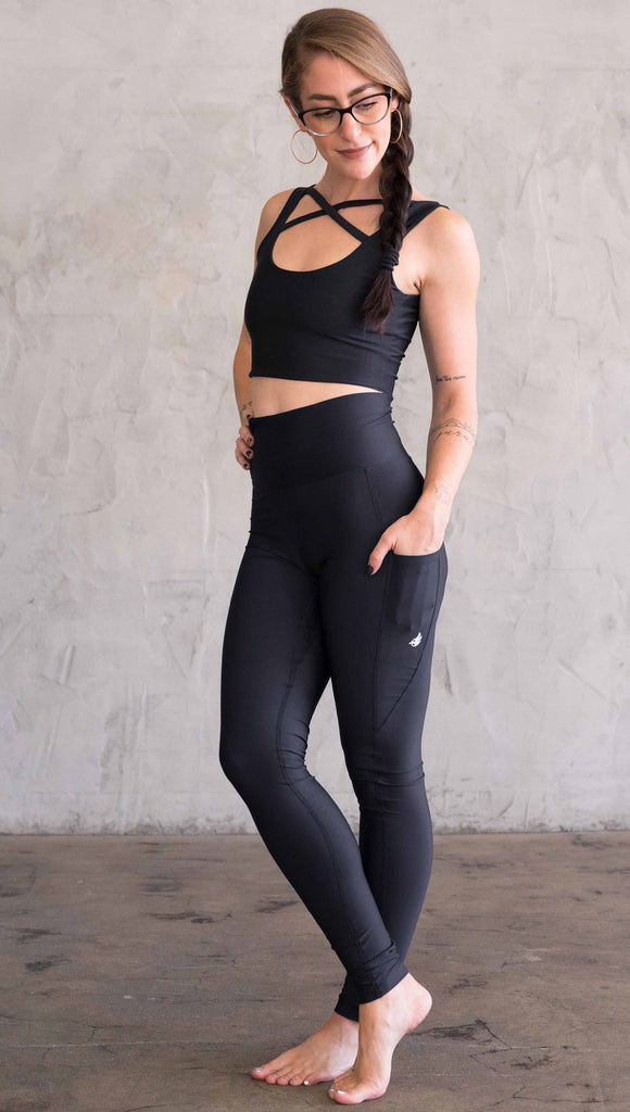 Full body view of model wearing WERKSHOP featherlight leggings. Leggings have a small reflective eagle logo on the wearer's left pocket.