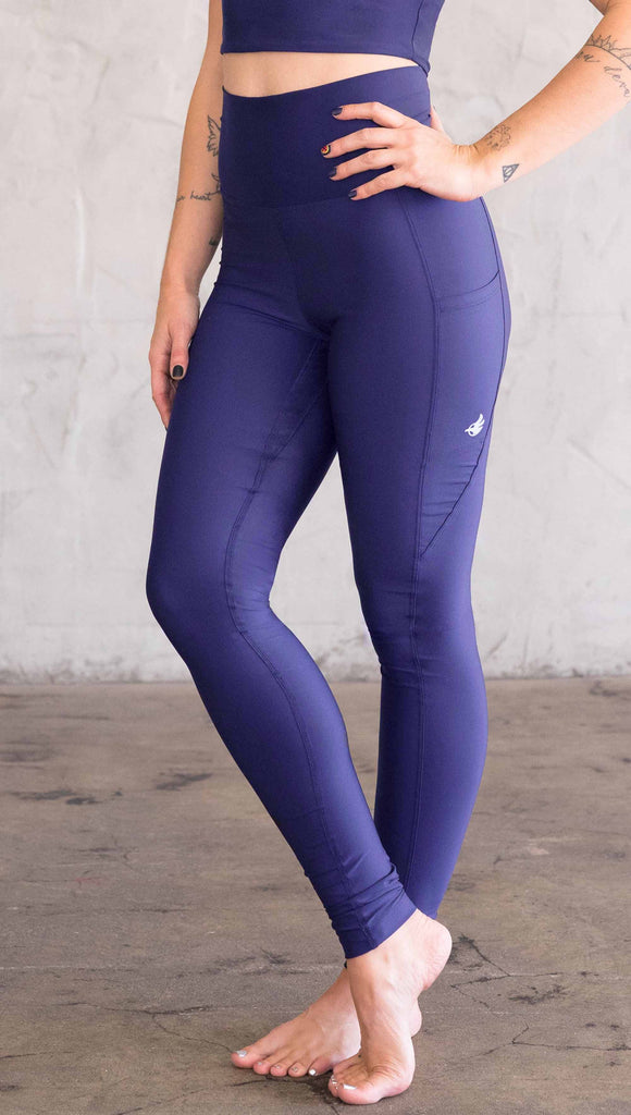 Model wearing WERKSHOP featherlight leggings in solid royal blue color. Leggings have a small reflective eagle logo on the wearer's left pocket.