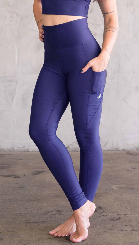 Model wearing WERKSHOP featherlight leggings in solid royal blue color. Leggings have a small reflective eagle logo on the wearer's left pocket.