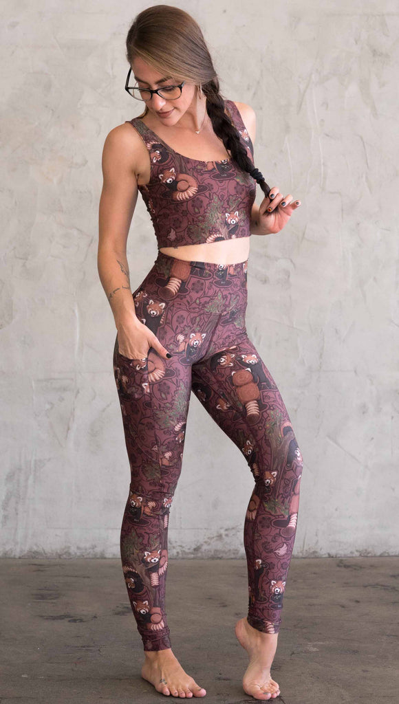 Side view of model wearing WERKSHOP Red Panda Leggings. The artwork is dark red with clusters of cute red pandas playing on trees. The leggings have phone pockets on both legs.