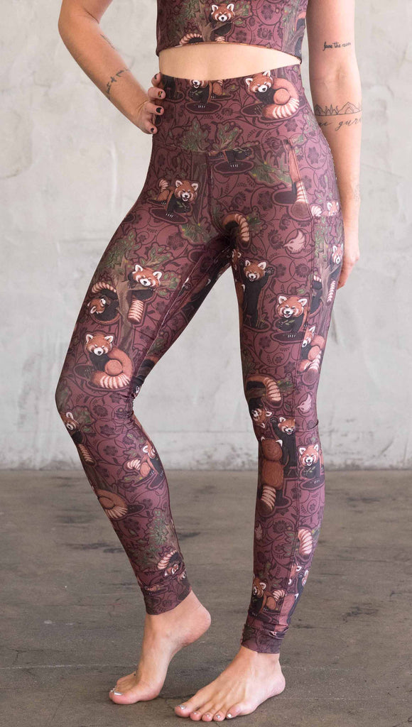 Front view of model wearing WERKSHOP Red Panda Leggings. The artwork is dark red with clusters of cute red pandas playing on trees. The leggings have phone pockets on both legs.