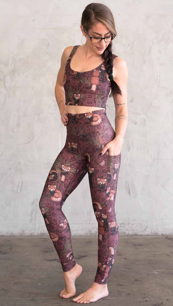 Front view of model wearing WERKSHOP Red Panda Leggings. The artwork is dark red with clusters of cute red pandas playing on trees. The leggings have phone pockets on both legs.