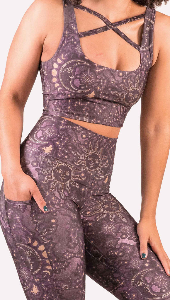 Model wearing WERKSHOP Zodiac Leggings. They are high waist and feature pockets on both legs. The zodiac themed artwork shows a hand-drawn sun and moon with the moon phases, shooting stars and all 12 zodiac constellations in gold over a dark purple background.