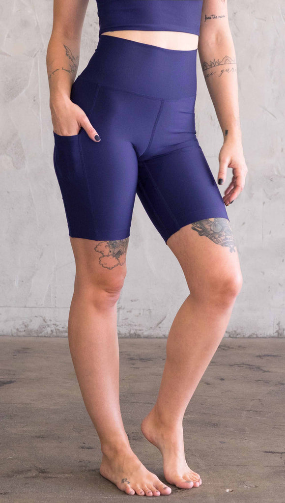 Model wearing WERKSHOP bicycle length shorts in featherlight fabric. Navy color with side cell phone pockets and a small eagle logo on the wearers left side