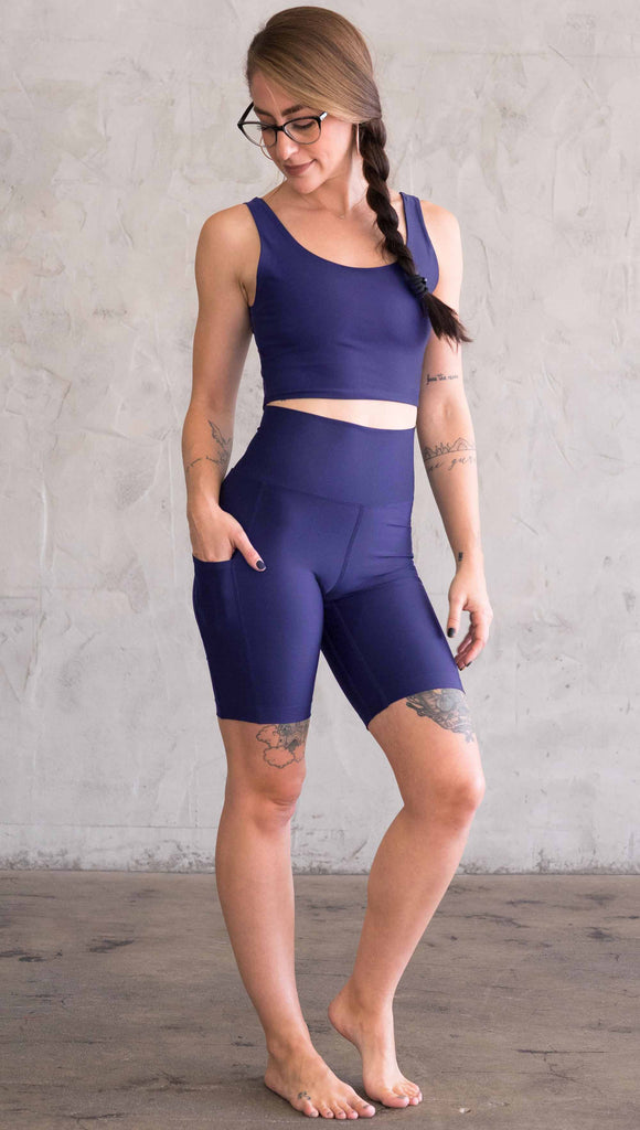 Model wearing WERKSHOP bicycle length shorts in featherlight fabric. Navy color with side cell phone pockets and a small eagle logo on the wearers left side