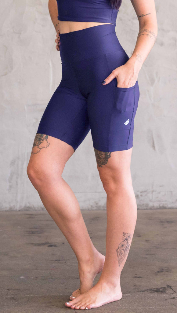 Model wearing WERKSHOP bicycle length shorts in featherlight fabric. Navy color with side cell phone pockets and a small eagle logo on the wearers left side