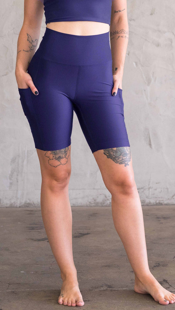 Model wearing WERKSHOP bicycle length shorts in featherlight fabric. Navy color with side cell phone pockets and a small eagle logo on the wearers left side