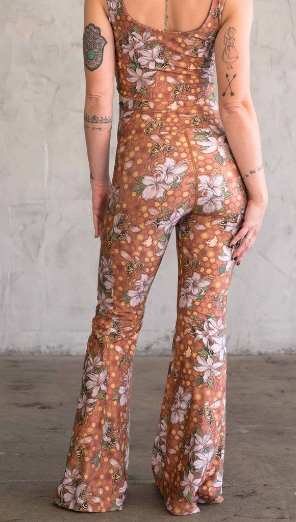 Back view of model wearing WERKSHOP Honeybee Bell Bottoms. The leggings have clusters of honeybees and flowers and phone pockets on each leg