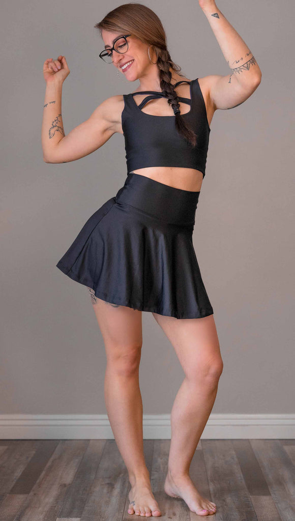 Full body view of model wearing WERKSHOP Tennis Skirt. In solid black color