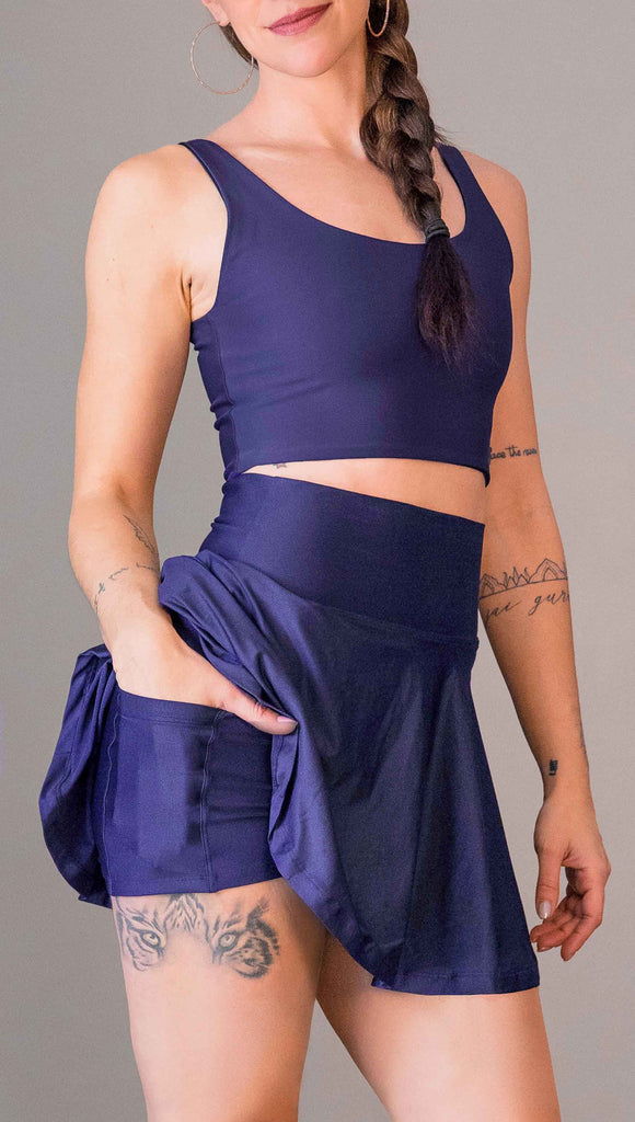 model wearing WERKSHOP Tennis Skirt, with the skirt lifted up to show the shorts and pockets underneath. In solid royal blue color