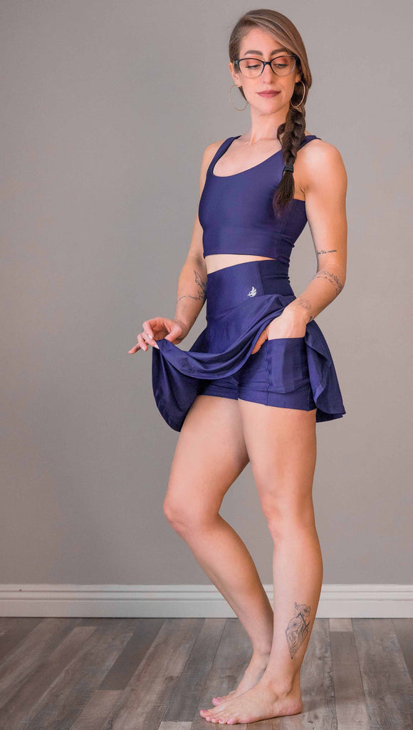 model wearing WERKSHOP Tennis Skirt, with the skirt lifted up to show the shorts and pockets underneath. In solid royal blue color