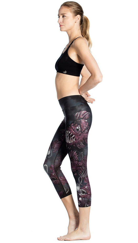 left side view of model wearing deep sea angler fish printed capri leggings and black sports top