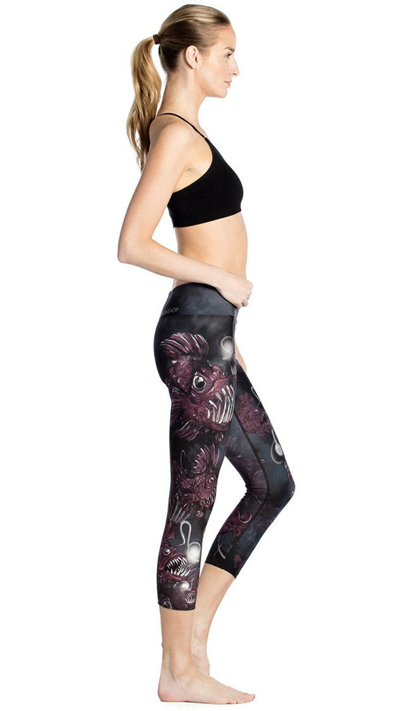 right side view of model wearing deep sea angler fish printed capri leggings and black sports top