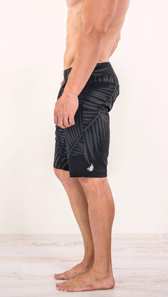 Close up right side view of model wearing tropical palm fronds printed men's performance shorts