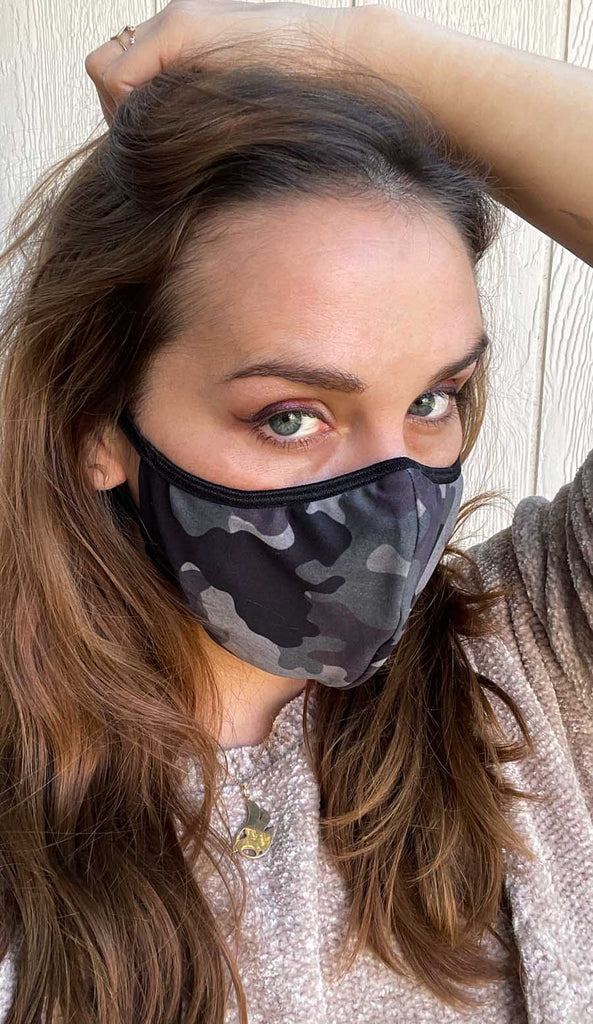 Girl wearing WERKSHOP Camo Face Mask - classic green and brown colors with an orange logo and adjustable ear loops.