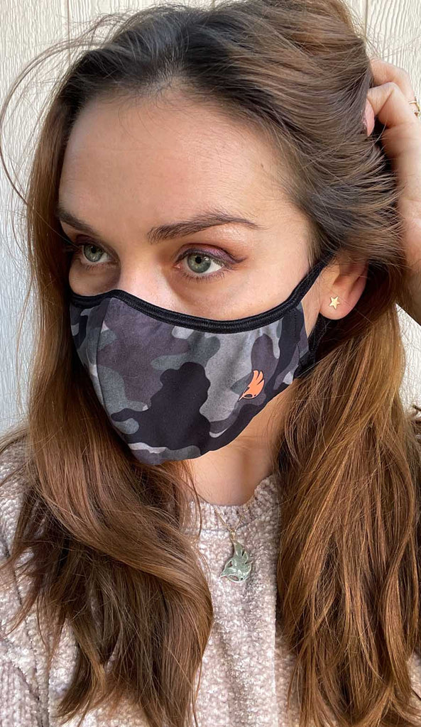 Girl wearing WERKSHOP Camo Face Mask - classic green and brown colors with an orange logo and adjustable ear loops.