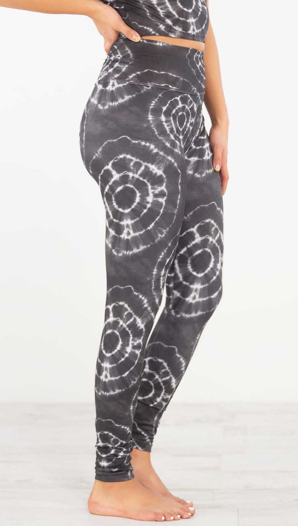 Right side view of model wearing the charcoal athleisure leggings. They are in a charcoal color and have white tie dye circles throughout. Each circle has a smaller circle within each other.