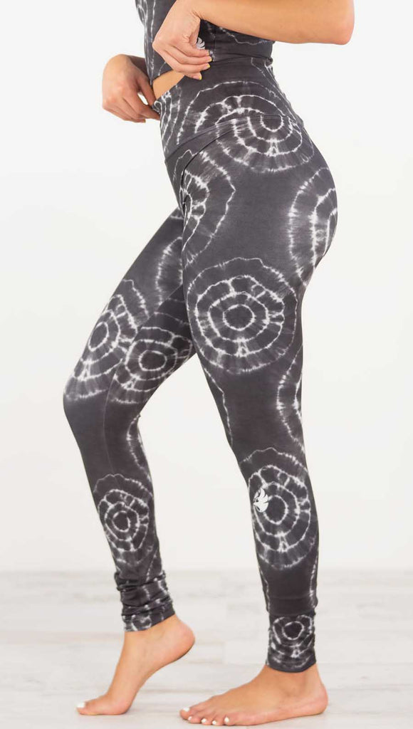 Left side view of model wearing the charcoal athleisure leggings. They are in a charcoal color and have white tie dye circles throughout. Each circle has a smaller circle within each other.