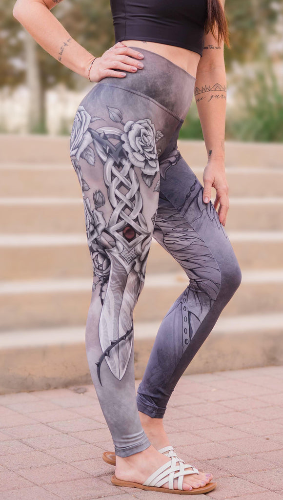 Model wearing WERKSHOP Dagger Mashup Leggings. One leg has a dagger with a wreath of roses. The other leg has an abstract gargoyle-esc dragon. Both legs are neutral in color tone with the right leg being a bit taupe and the left leg being a cool gray.