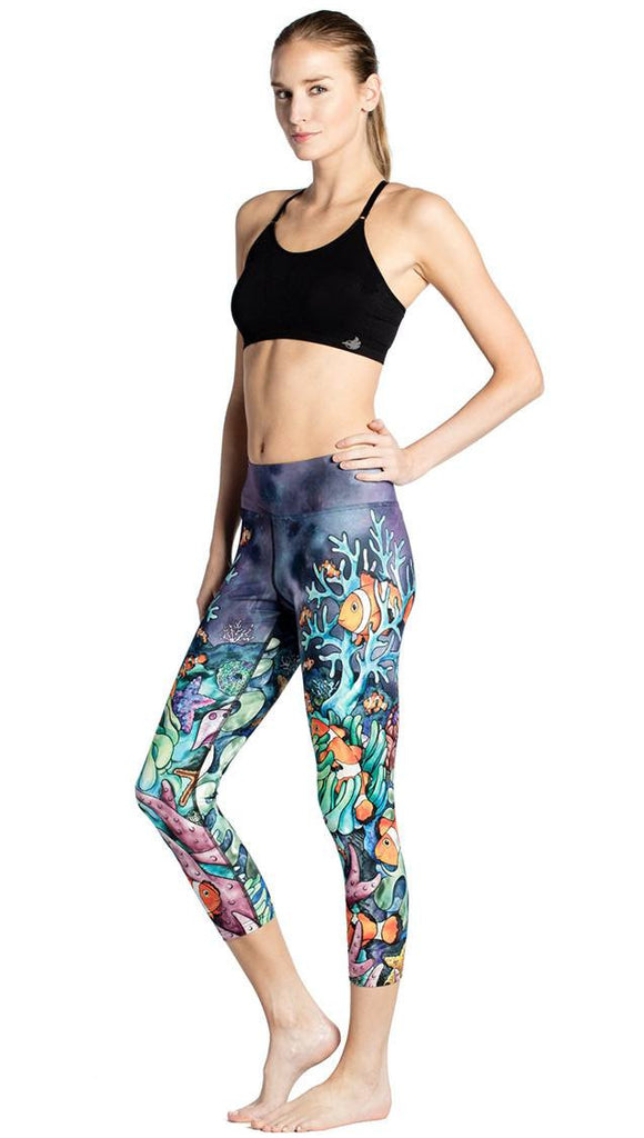 slightly turned front view of model wearing coral reef themed printed capri leggings