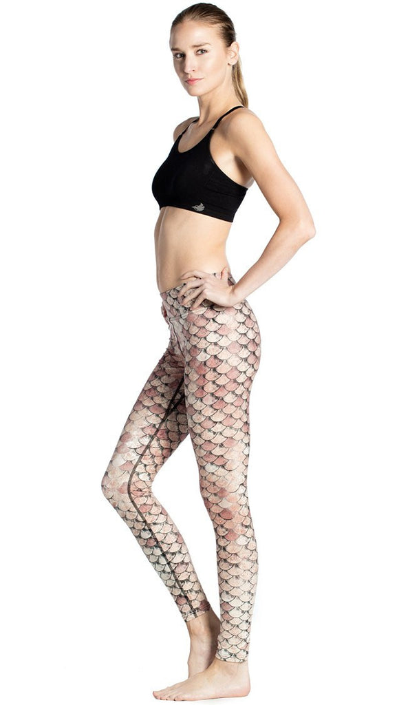 left side view of model wearing gold mermaid scale themed printed full length leggings