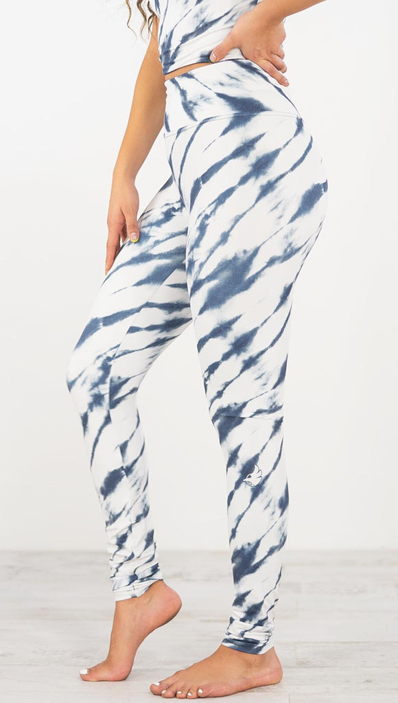 Left side view of model wearing the indigo stripes athleisure leggings. They are in a white color and have blue zebra-like stripes.