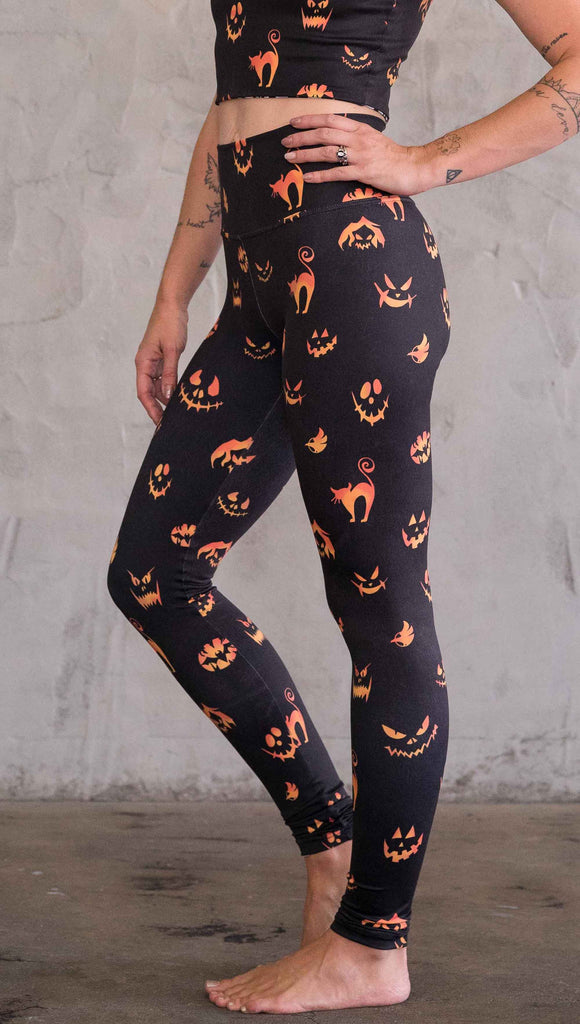 Left view of model wearing the black athleisure leggings with bright orange jack-o-lantern faces and cats throughout