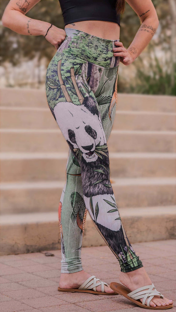 Model wearing WERKSHOP Koi Fish and Giant Panda Mashup Leggings. The wearer's right leg has an illustration of a panda eating bamboo with a gorgeous background of mountains. The wearers right leg has koi fishies swimming over an abstract taupe and forest green background.