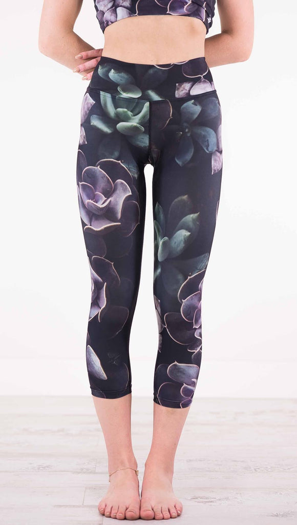 Front view of model wearing black capri leggings with green and purple succulent plants throughout