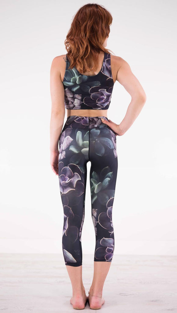 Back view of model wearing black capri leggings with green and purple succulent plants throughout